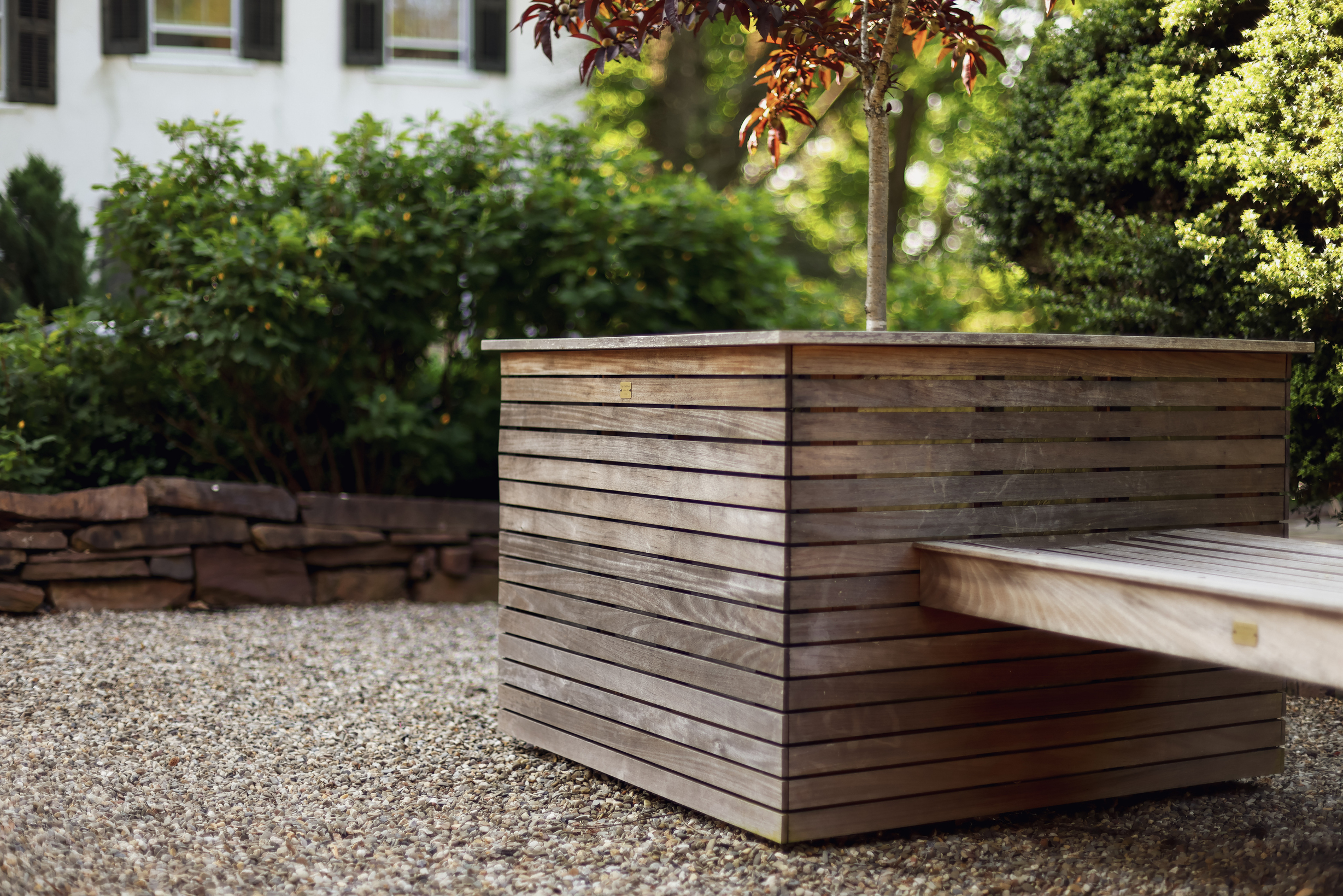 wooden square planter with green flower coming out, bench next to it